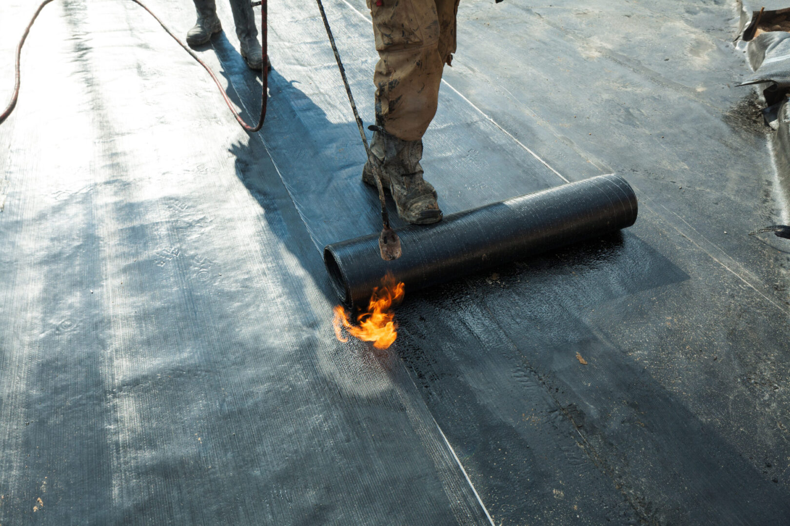 A roofer installs a roll roofing of waterproofing propane with a blowtorch.