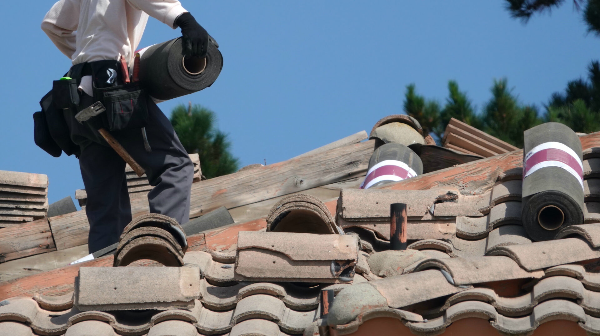 Roofer carries roofing material across a roof under repair