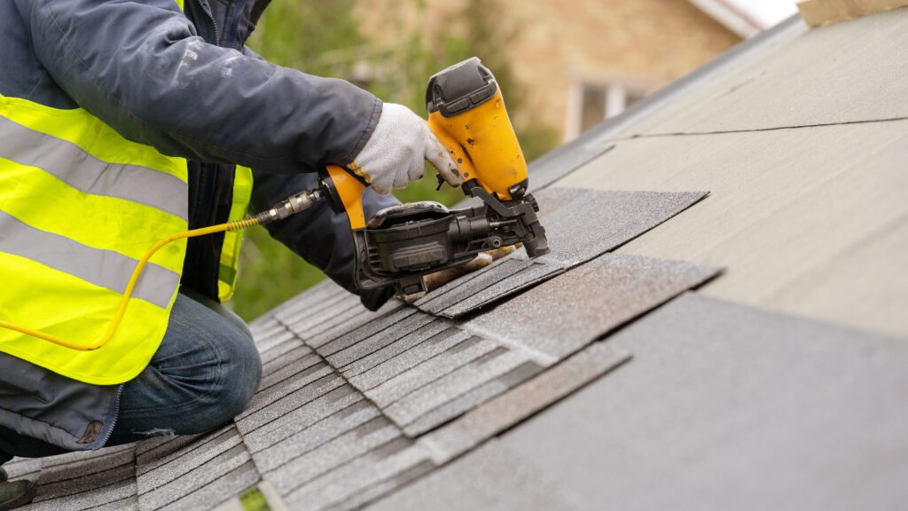 A worker operating a nail gun on a roof while making a residential roof repair