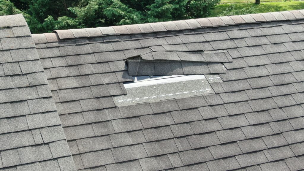 A gray asphalt shingle roof with shingles blown up